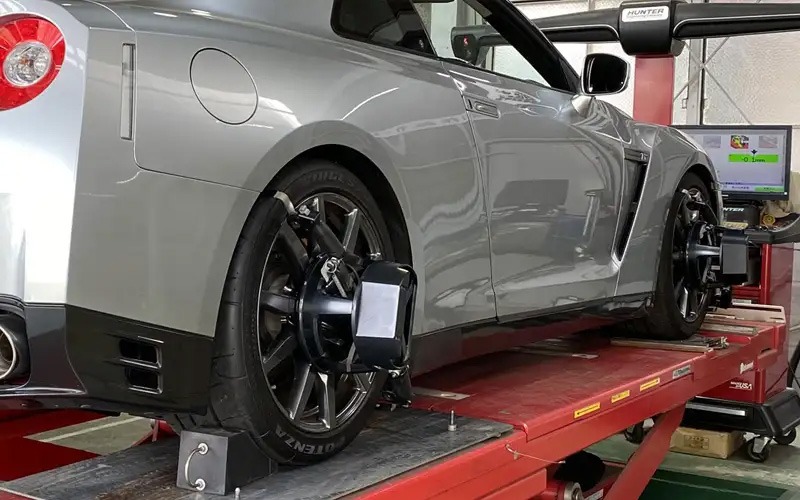Silver sports car on a raised workshop lift, with wheel clamps attached to the wheels for diagnostic testing.