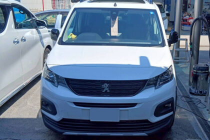 Front view of a white Peugeot van in a service bay, with workshop equipment in the background and another white car beside it