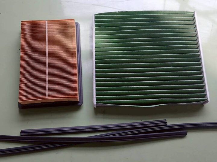 06 - 鈑金塗装・カーコーティング・車検|山口県周南市 東洋ボデー株式会社 Two pleated air filters on a pale green surface: a small orange filter and a larger green one, with several black strips laid out nearby.