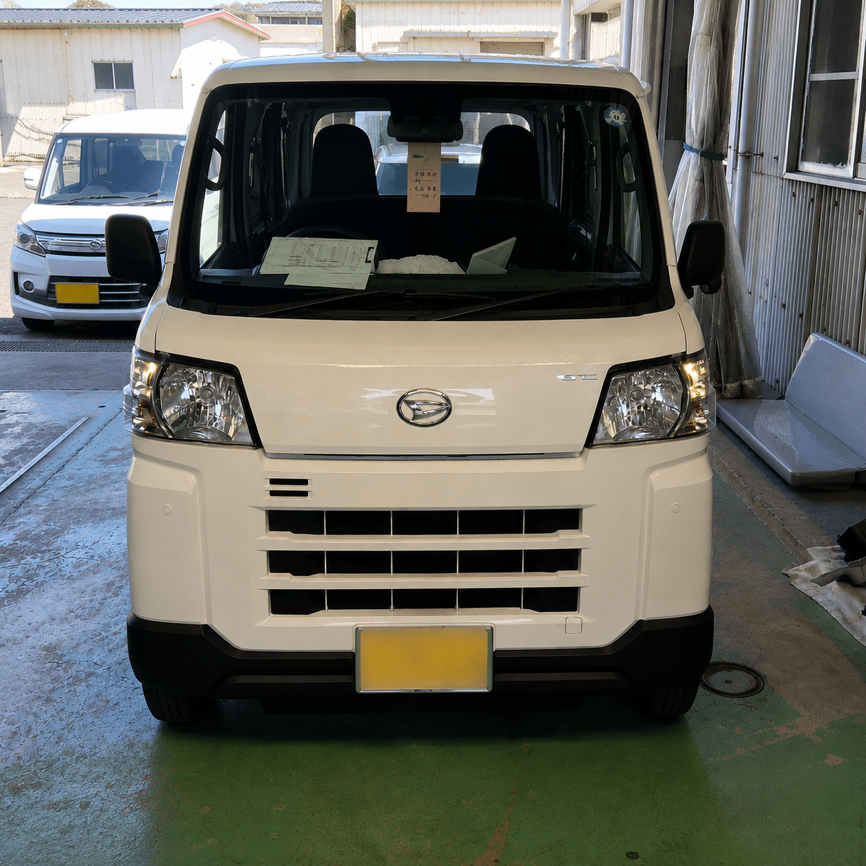 Front view of a white van in a service bay, with papers on the dashboard and a yellow license plate.